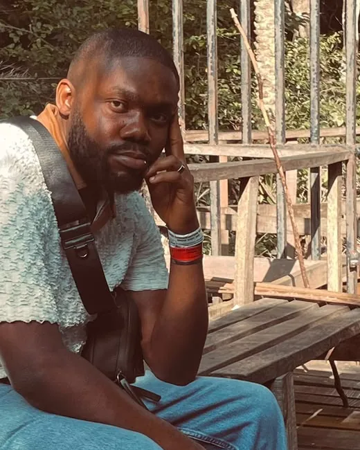 Henry Ifebunandu sitting on a wooden boardwalk among trees, chin resting on his hand